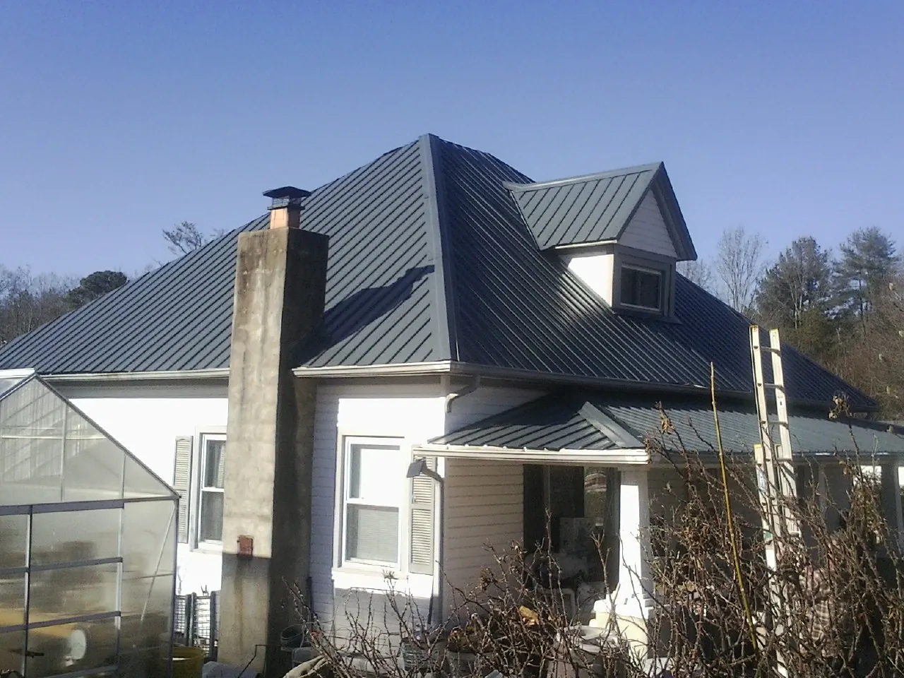 Dark blue standing seam metal roof on a white farmhouse with dormer — Slate & Tile Roof Repair by Roofing Brothers in Greenport