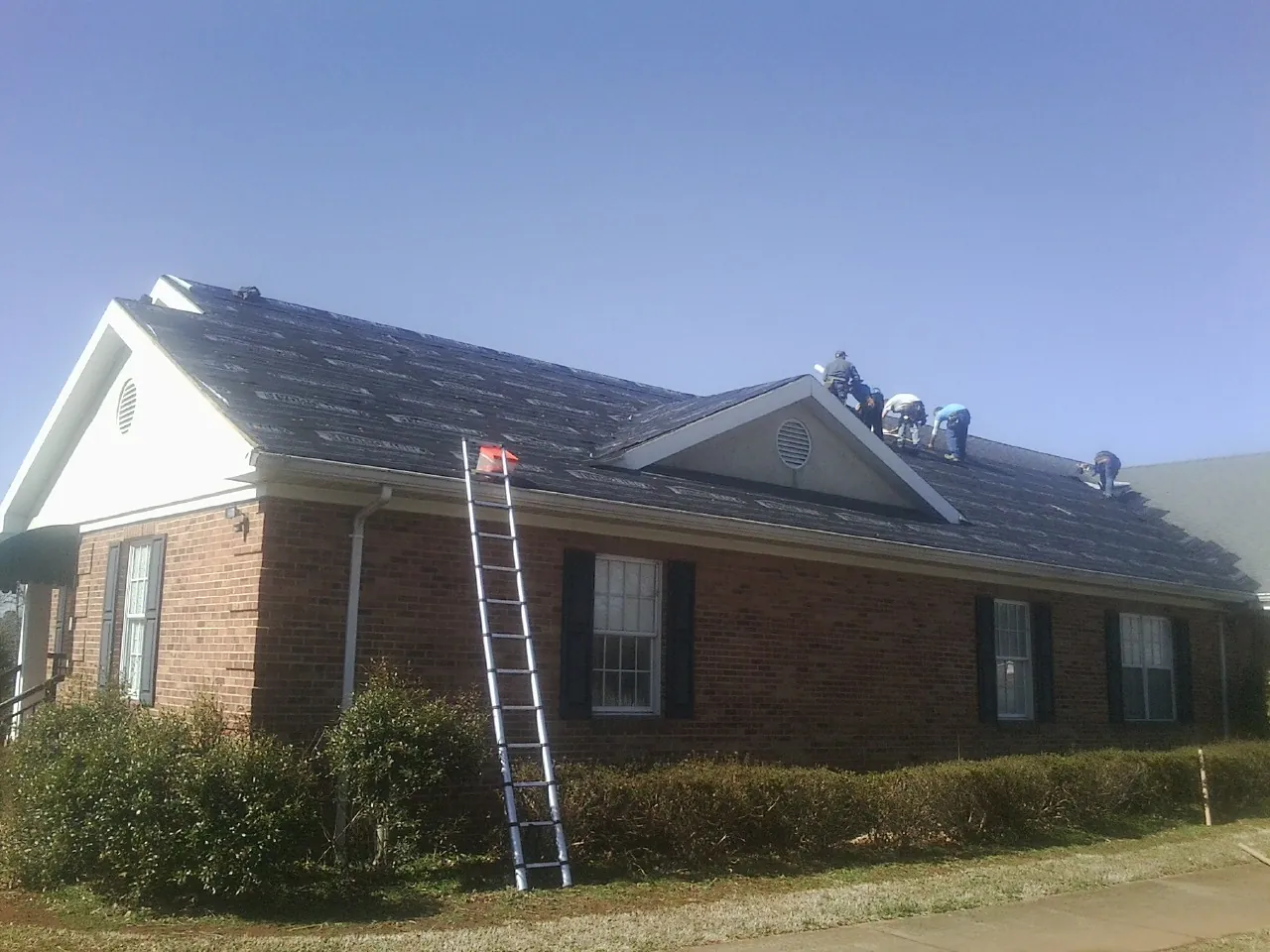 Crew tearing shingles off a brick ranch roof with a ladder set — Emergency Roof Repair work by our crew in Greenport