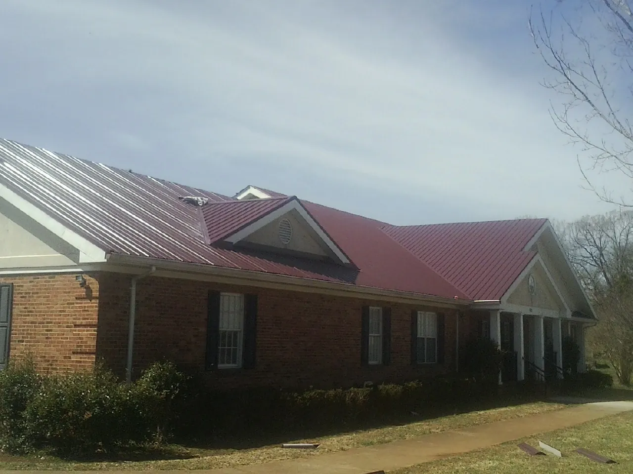 Red metal roof with gabled entries on a long brick building, from a Hail Damage Roof Repair job in Greenport