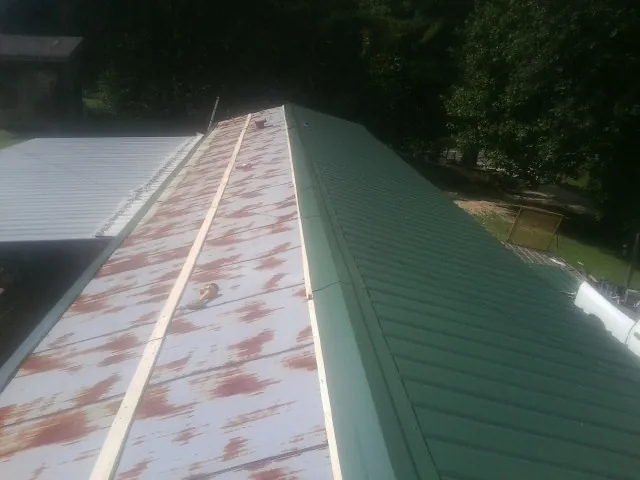 Old rusted panels beside newly installed green metal roofing in Greenport