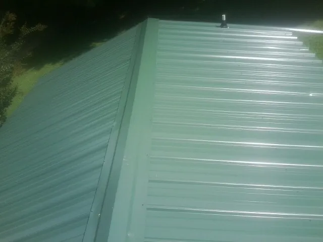 New green metal panels meeting at the ridge of a roof — Flat Roof Repair work by our crew in Greenport