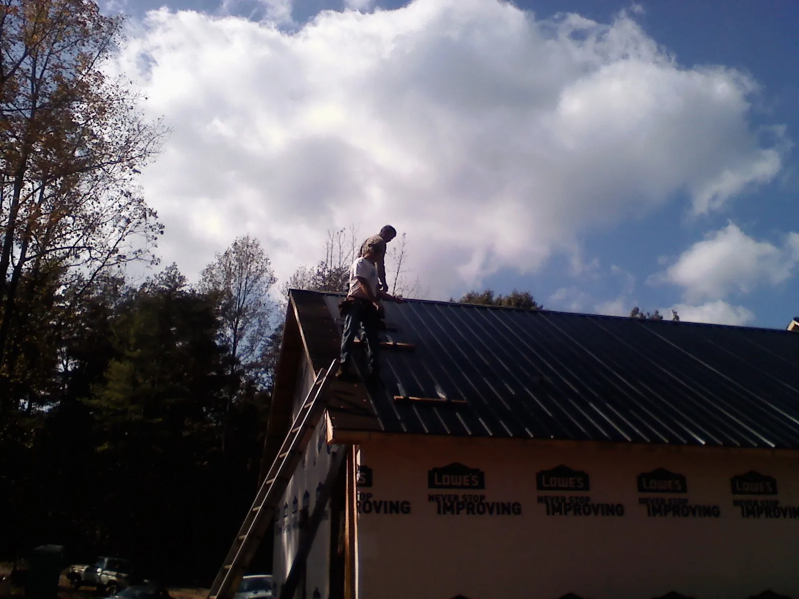 Roofer fastening dark metal panels high against a cloudy sky, from a Roof Inspection job in Greenport