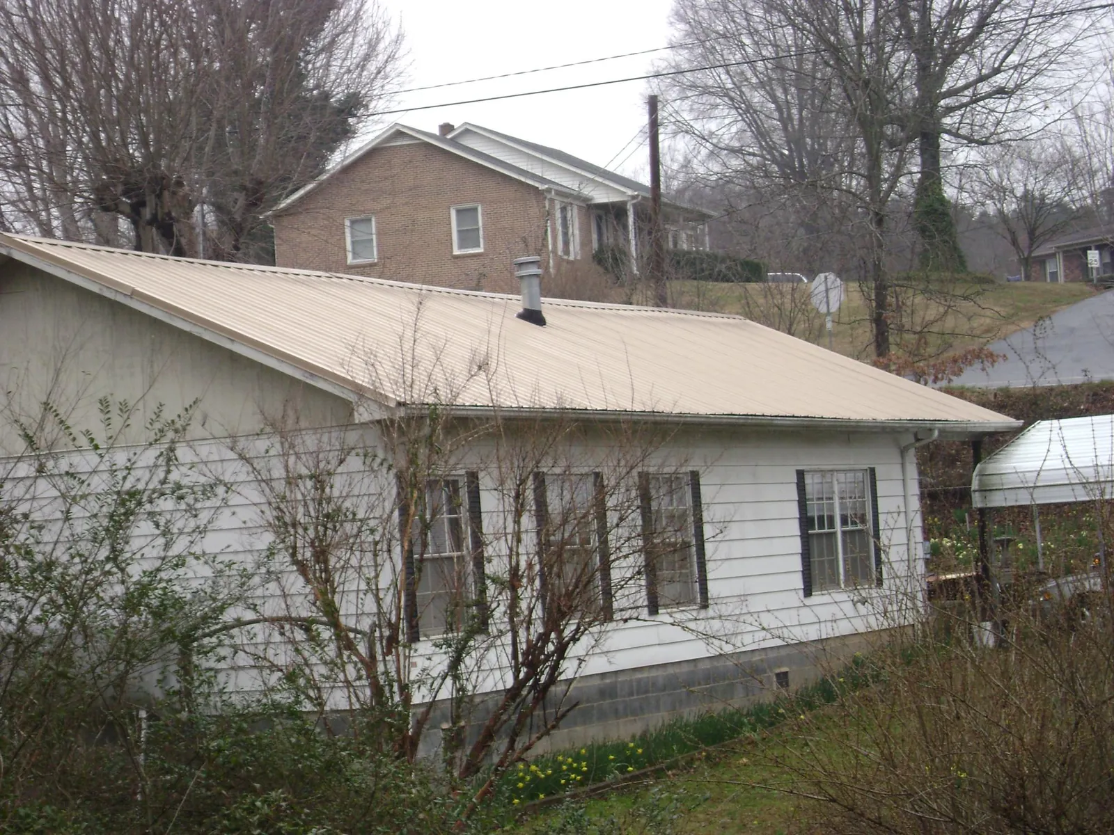 Tan metal roof on a white sided house set into a hillside — Commercial Roofing by Roofing Brothers in Greenport